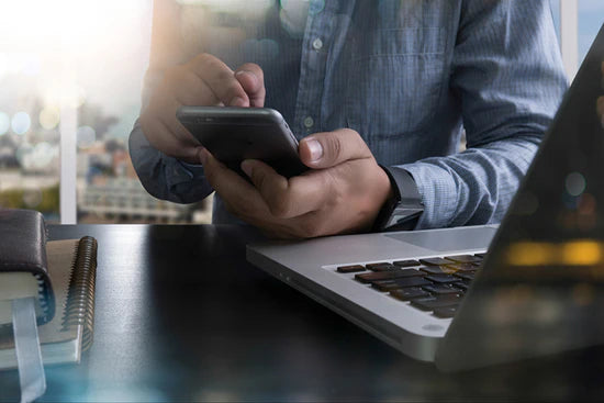 Man typing on phone with a laptop next to him symbolizing the digital marketing and retailer support tools from ABS – Art Brand Studios Wholesale Marketing Resources.