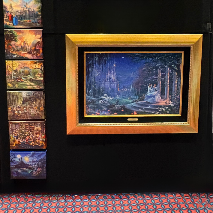 Wall showcasing a variety of canvas paintings and a canvas in a frame, showing Cinderella dancing.